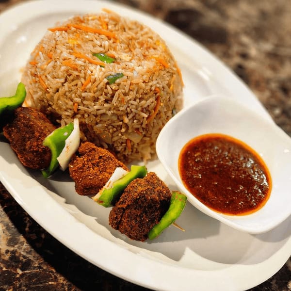 Safari77 Cuisine's African dish with seasoned rice, meat skewers with peppers and onions, and a side of red sauce.